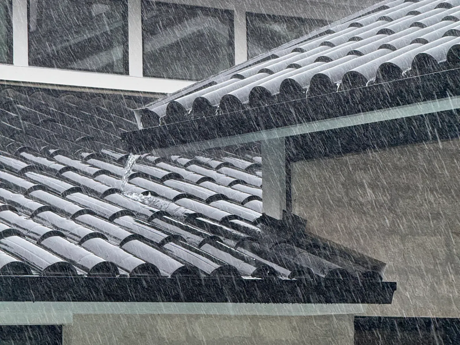 Heavy rain sheeting off a tile roof into the gutter line on a Central Texas home